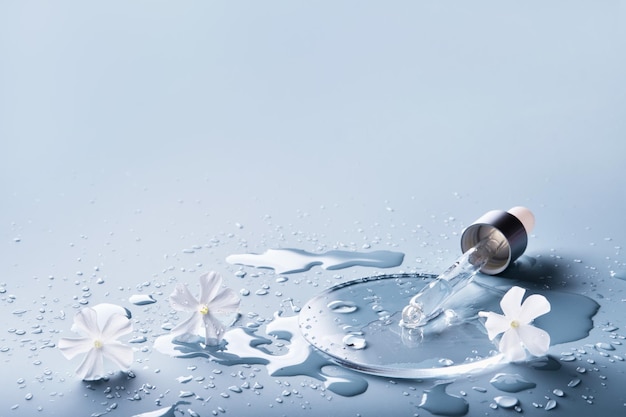 Pipette cosmetic product and White flowers in glass slide on blue background selective focus