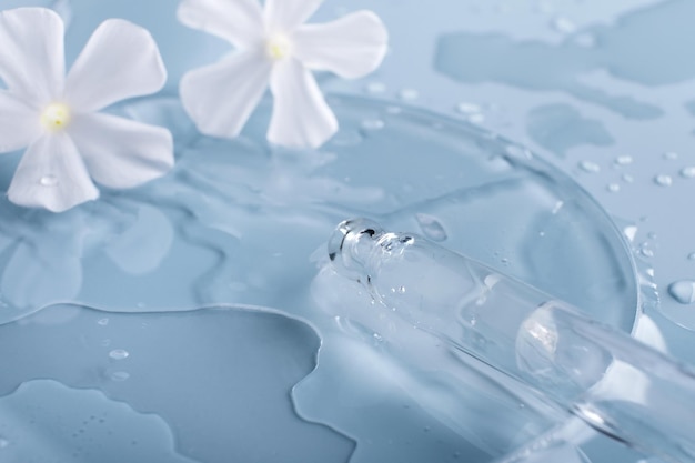 Pipette cosmetic product and White flowers in petri dish on blue background selective focus