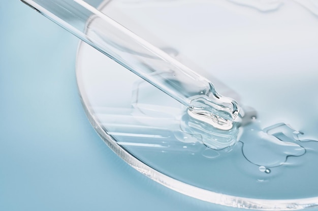 Pipette with sample of cosmetic product in petri dish on blue background selective focus