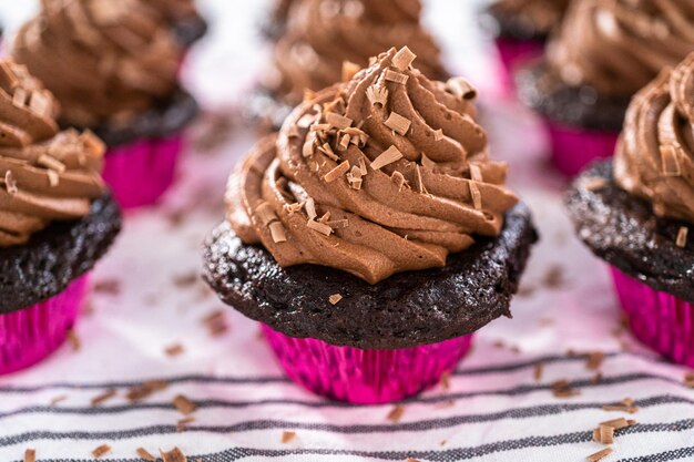 Piping chocolate ganache frosting on top of chocolate cupcakes.