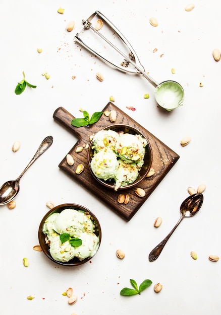 Pistachio ice cream with nuts decorated with mint leaves in brown bowls light background top view