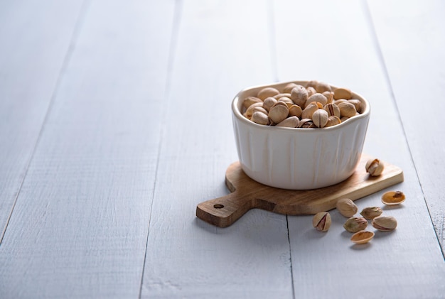 Pistachio nuts in a white bowl on a light wooden background. Front view and copy space image