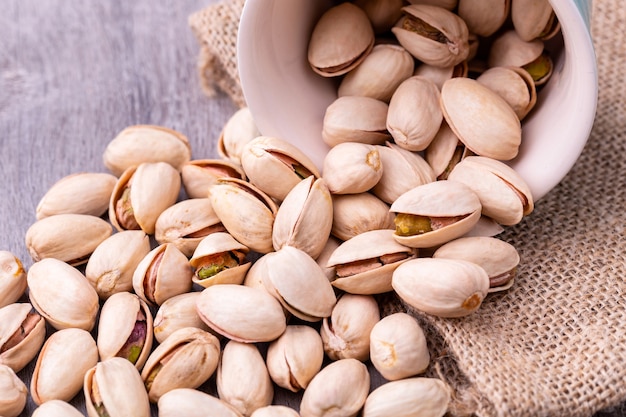 Pistachio nuts in a white ceramic bowl on a wooden table.