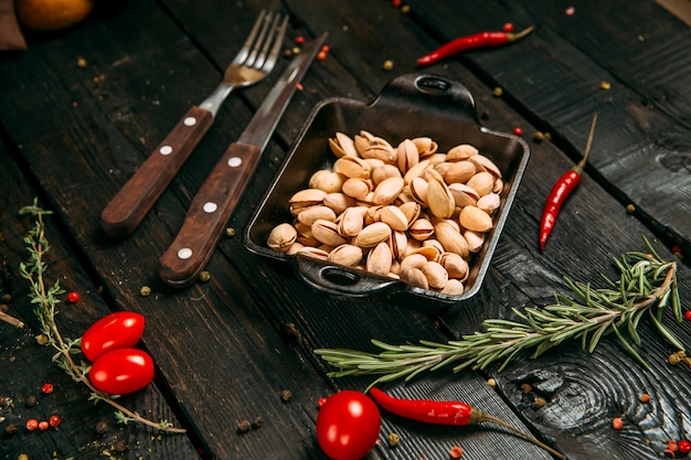 Pistachios in a black bowl on the dark wooden background, side view, horizontal