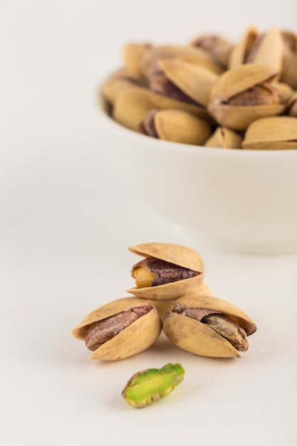 Pistachios close-up on a light background and in a white bowl. A natural product for the diet. Side view with a copy space. Vertical orientation.