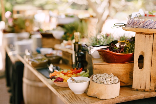 Pistachios in a wooden bowl on a table with salads on a blurred background