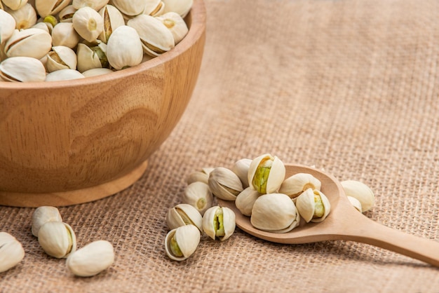 Pistachios in wooden spoon and wooden bowl.