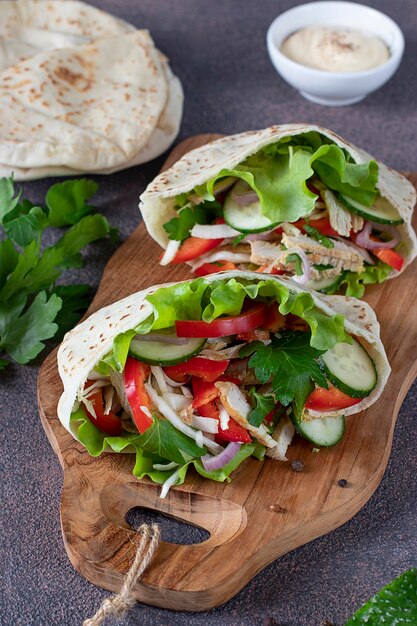 Pita stuffed with chicken, pepper, cucumber and lettuce on wooden board. Middle Eastern cuisine. Vertical format