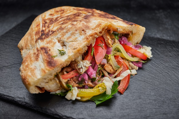 Pita with meat and vegetables, pork, cabbage, tomatoes, pickles, on slate, on a black background