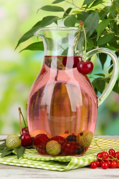 Pitcher of compote with summer berries on natural background