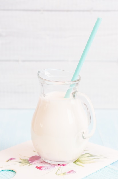 Pitcher glass of milk with lavender and cocktail tube on a blue wooden background