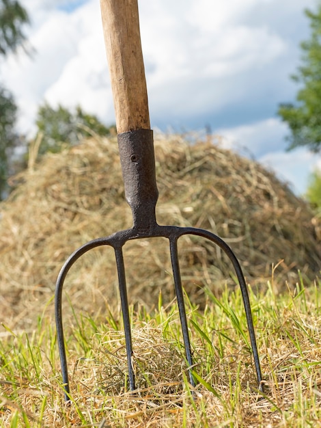 Photo a pitchfork for agriculture is stuck in the ground against the background of a haystack.