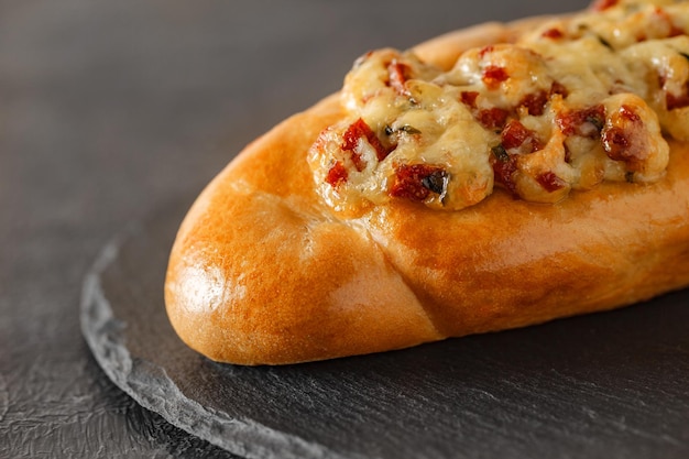 Pizza on baguette bread with salami and melted cheese on slate stone plate round dark background selective focus