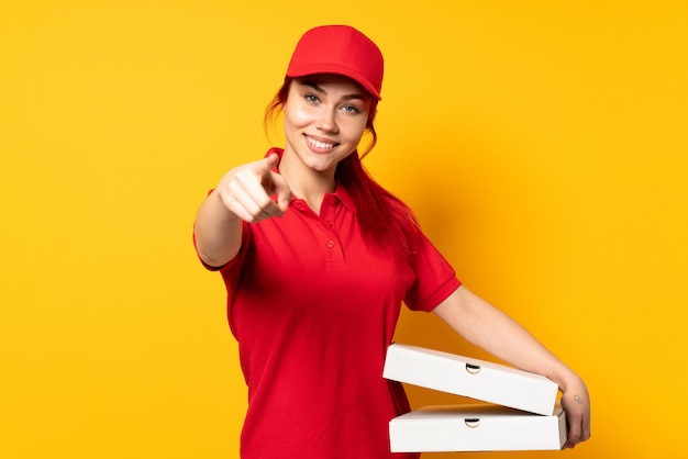 Pizza delivery girl holding a pizza over isolated background pointing front with happy expression