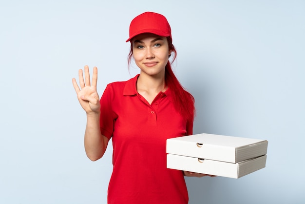 Pizza delivery girl holding a pizza over isolated wall happy and counting four with fingers