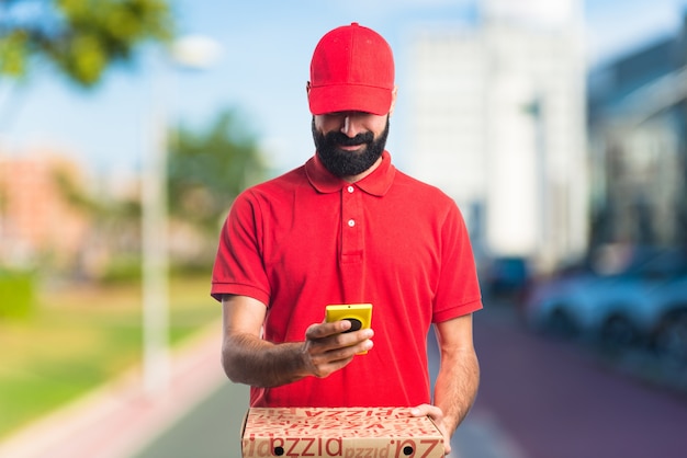 Pizza delivery man holding a mobile on unfocused background