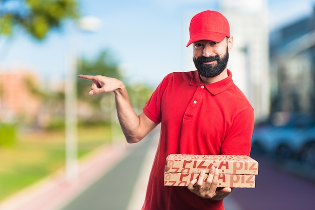 Pizza delivery man pointing to the lateral on unfocused background