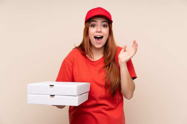 Pizza delivery teenager woman holding a pizza with surprise facial expression