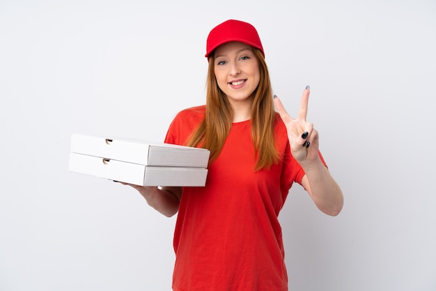 Pizza delivery woman holding a pizza over isolated pink wall smiling and showing victory sign