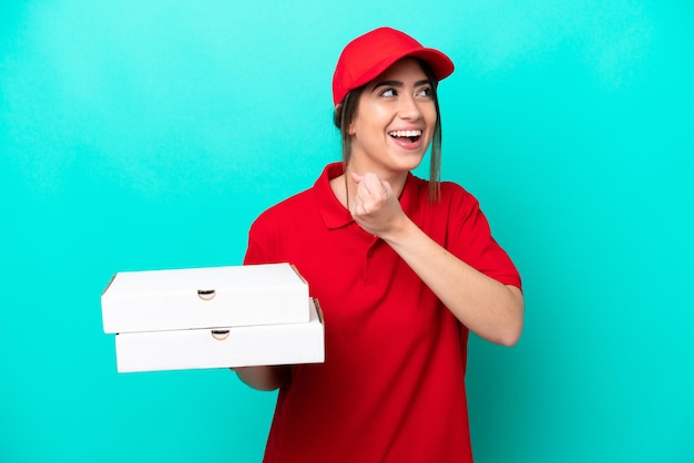 Pizza delivery woman with work uniform picking up pizza boxes isolated on blue background celebrating a victory