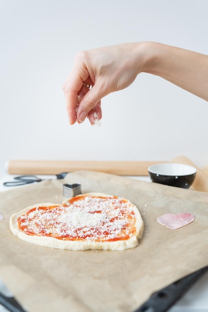 Pizza dough in the shape of a heart the chef sprinkles the pizza with parmesan cheese The concept of a surprise for St Valentine's Day