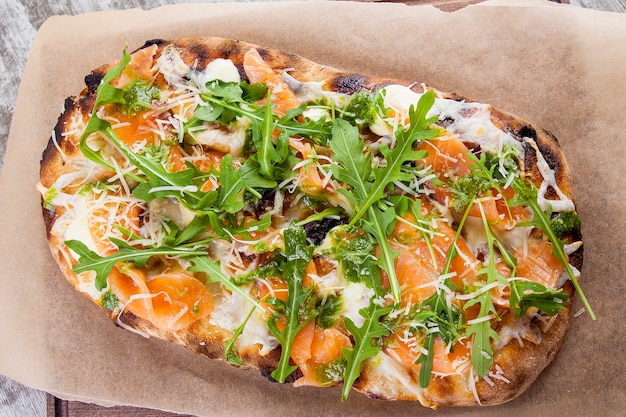 Pizza on a fluffy dough with lightly salted salmon cheese pesto sauce and arugula