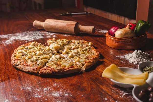 Pizza of hearts of palm cut in pieces next to the ingredients on a wooden table.