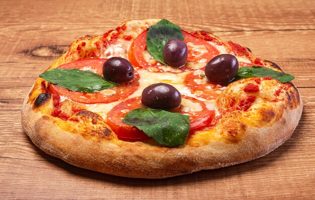 Pizza Margherita, with eggplant, tomato, basil leaves and black olives, served on a rustic wooden table.