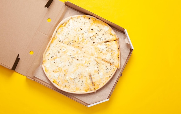 Pizza in an open box on yellow background Top view