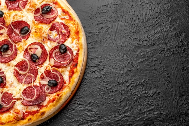 Pizza SALAMI on a black background, tomato-based with mozzarella, salami, onions and olives on a wooden stand