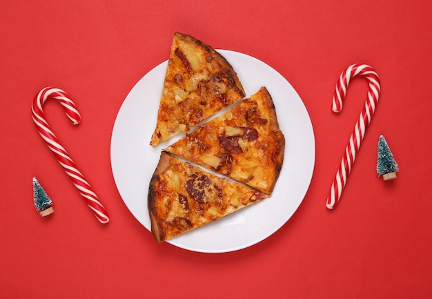 Pizza slices on plates and Christmas decor Christmas trees and candies Red background