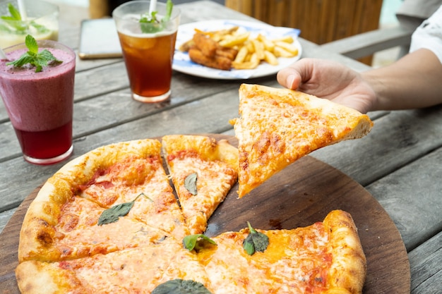 A pizza on the table taken a piece with hands and fresh juice