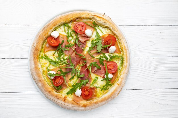 A pizza with arugula, mozzarella, and mozzarella on a white wooden table.