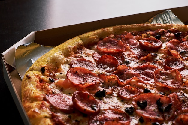 Pizza with bacon in a cardboard box on a dark background. Close-up. View from above. Pizza delivery