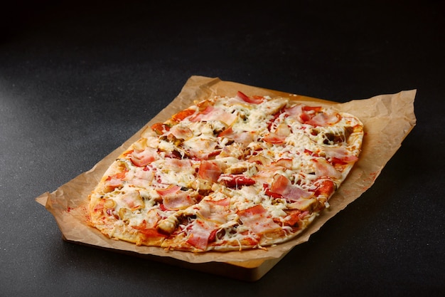 Pizza with bacon, vegetables and sauce on dark concrete table