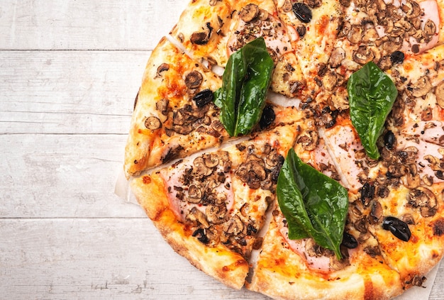 Pizza with ham and mushrooms on a white wooden table.