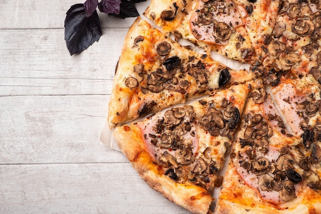 Pizza with ham and mushrooms on a white wooden table