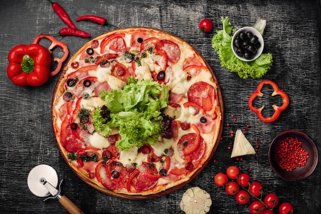 Pizza with ham, salami, cheese, mushrooms, cherry tomatoes, bell peppers and salad on a black chalk board.