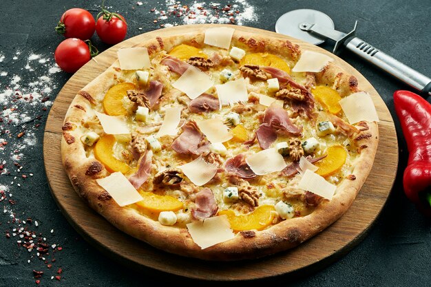 Photo pizza with a large number of toppings: jamon, parmesan, nuts, blue cheese and peaches. pizza in composition with ingredients on a black table