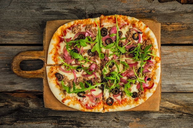 Pizza with minced meat, black olives, onion, rocket salad, cheese and tomato sauce, on wooden board