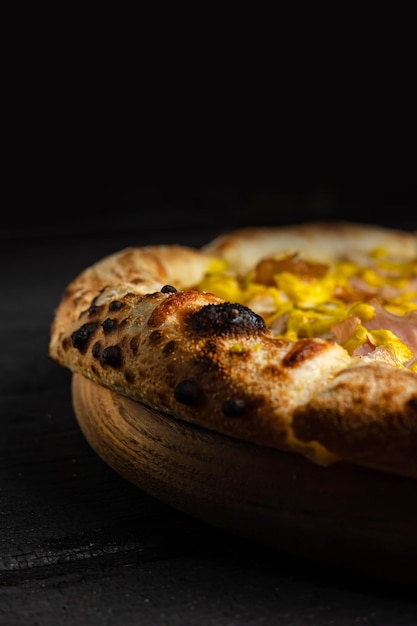 A pizza with pineapple on it sits on a wooden plate.