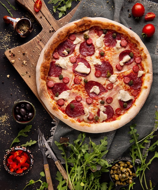 Pizza with salami, mozzarella cheese, capers and sausages on the wooden cupboard