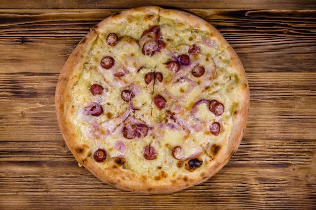 Pizza with sausages, ham and parmesan cheese on a wooden table. Top view