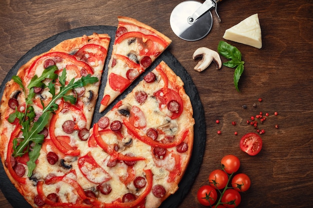 Pizza with smoked sausages, cheese, mushrooms, tomatoes, bell peppers on a stone and a wooden brown board.