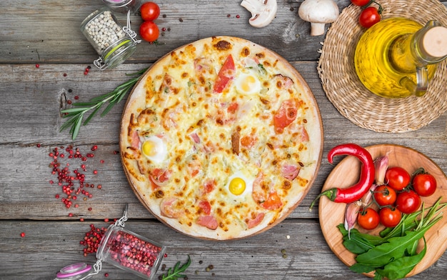 Pizza with tomatoes, mozzarella cheese, black olives and basil. Delicious italian pizza on wooden pizza board. Table top view