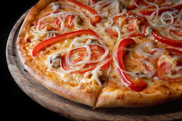 Pizza on a wooden board, with pepper, onions, chicken, cheese and tomatoes, on a black background,partially photographed