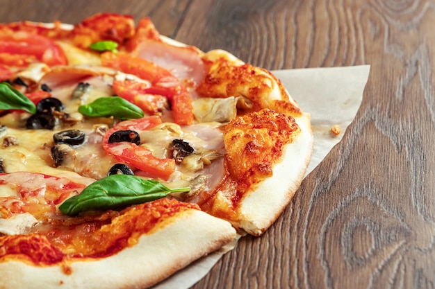 Pizza on wooden with ham, olives, tomatoes and green basil