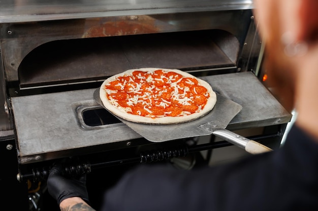 Photo pizzaiolo takes the finished pizza out of the electric oven ppizzaiolo holds a pizza on a spatula