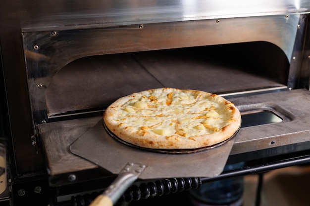 Photo pizzaiolo takes the finished pizza out of the electric oven ppizzaiolo holds a pizza on a spatula