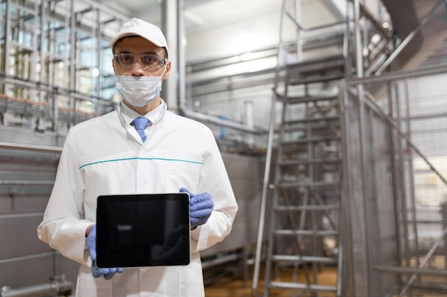 Place for writing The technologist in a mask gloves and a white robe stands with a tablet with an empty screen at the factory A man with a digital tablet in uniform in the production shop